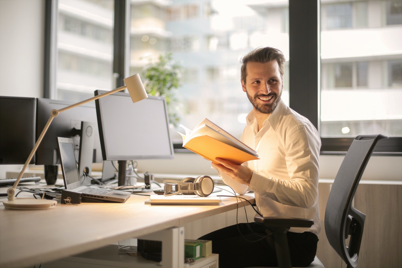 Smiling man holding a book in an office